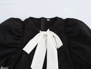 Detail eines schwarzen Jacquard-Minikleids mit Puffärmeln und weißer Schleife
