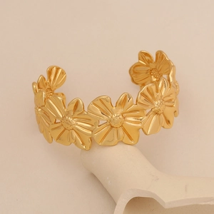 Gros plan d'un bracelet ouvert à fleurs dorées exposé sur un support en pierre