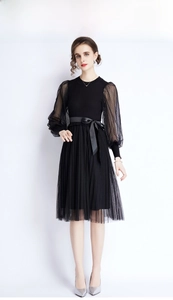 Detail of elegant black knit dress with polka dot mesh sleeves and pleated skirt