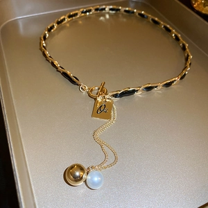 Detail of gold metal necklace with black faux leather braid, pearl and square pendant