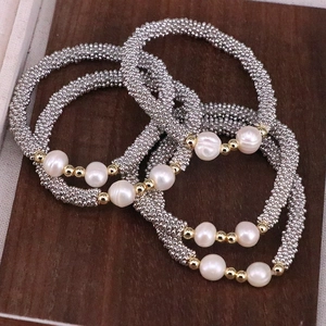 Detail of beaded bracelet set with white pearls and silver textured beads on wooden surface