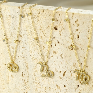 Detailed close-up of gold plated zodiac necklaces with cubic zirconia on beige stone