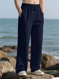 Detail of navy blue pleated wide-leg trousers with drawstring waist on coastal rocks