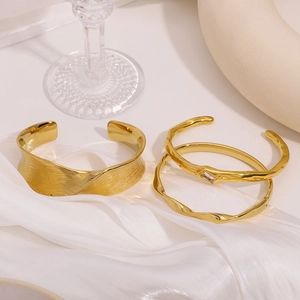 Three-piece gold cuff bracelet set with zircon stones on white silk background