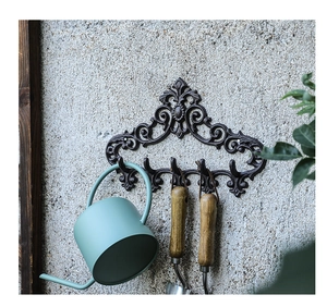 Detail of vintage cast iron wall rack with five hooks holding garden tools on cement wall
