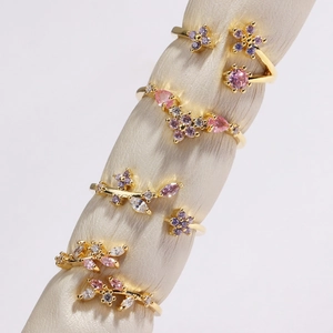 Détail macro de bagues dorées avec breloques fleurs et feuilles en zircon rose et violet