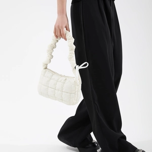 White ruched cloud handbag featuring quilted pattern and ruffled strap held by a model