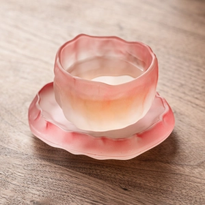 Pink frosted glass glacier tea cup with irregular edges on a rustic wooden table