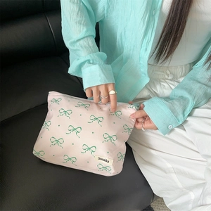 Close-up of floral makeup bag with pink fabric and green bow patterns held by a hand