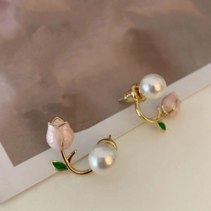 Detail of pink tulip earrings with gold leaves and a white pearl on a beige surface