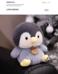 Close-up of a soft grey penguin plush toy with a wooden tag on a cozy leather surface