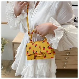 Detail van gele crossbodytas met aardbeienprint, gebogen basis en litchi lederen textuur