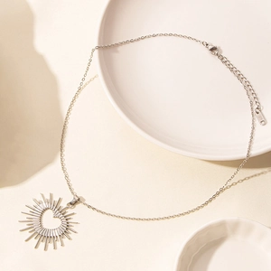 Detail of silver heart sun pendant on minimalist chain over elegant white ceramic plates