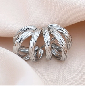 Detailed close-up of silver C-shaped twisted ribbed earrings on pink silk background