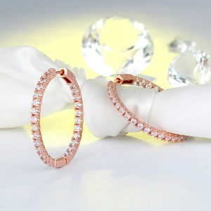 Macro detail of rose gold hoop earrings with pavé cubic zirconia on white silk