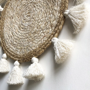 Vista macro di decorazione murale rotonda in erba intrecciata con nappe in cotone bianco