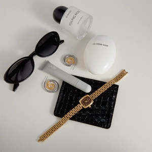 Flat lay of gold spiral earrings, quartz watch, and accessories on minimalist beige surface