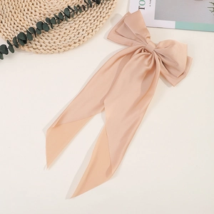 Detail of elegant champagne satin bow hair clip with long ribbons on a creamy background