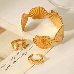 Detail view of gold seashell jewelry set including a wide bracelet and two open rings