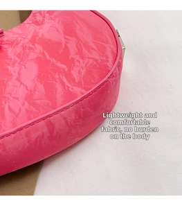 Detailed macro view of the glossy hot pink pleated leather texture on a crescent bag