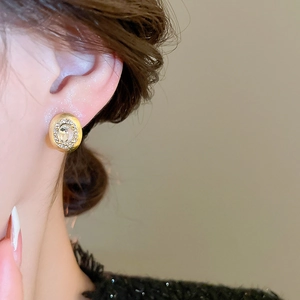 Close-up of golden brushed oval stud earrings with zircon inlay worn by a female model