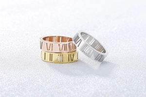 Macro detail of three cutout Roman numeral rings in rose gold, gold, and silver finishes