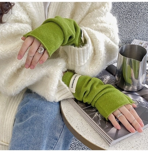 Close-up of green knitted fingerless gloves with a white nice moment tag on the wrist