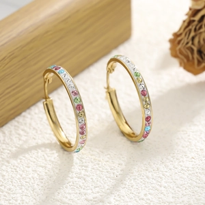 Macro shot of gold hoop earrings featuring colorful gemstones and white enamel inlay detail