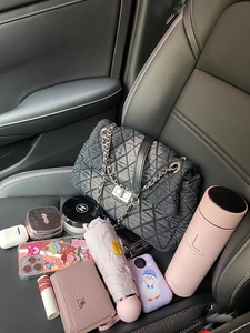 Interior view of large grey denim chain bag on leather car seat with everyday items
