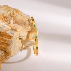 Gold plated stainless steel bangle featuring emerald green rectangular zircon stones