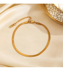 Close-up of golden stainless steel snake chain anklet on beige silk with ceramic dish