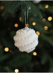 Detail of white textured Christmas ball with velvet pom-poms on a tree branch