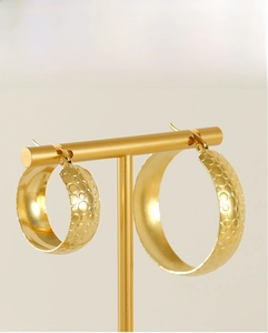 Detail of large 18K gold plated hoop earrings featuring a textured dot pattern on a stand