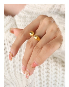 Close-up of golden geometric open ring with double sphere design on model wearing sweater
