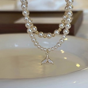 Macro shot of double-layer pearl bracelet with gold fishtail charm and micro-inlaid stones