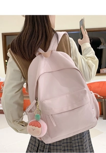 Close-up of a light pink nylon backpack featuring a soft plush charm and side pockets