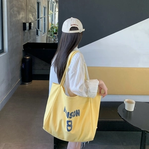 Woman carrying a large yellow canvas tote bag in a modern cafe setting from a side view