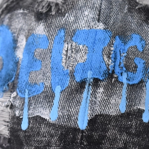 Macro view of washed denim cap showing blue spray graffiti and distressed edge details
