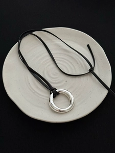 Macro shot of mirror-polished silver ring pendant on black leather cord necklace