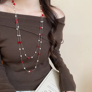 Detail of elegant double-layered necklace with red crystals and white pearls on a sweater