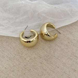 Flat lay of gold C-shape acrylic stud earrings on beige linen and crinkled paper