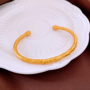 Detail of matte gold bangle with floral relief patterns on a ceramic shell plate
