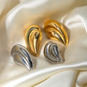 Detail of elegant gold and silver teardrop earrings resting on luxury champagne silk fabric