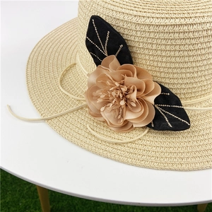 Detail shot of beige straw hat with khaki fabric flower and gold-lined black leaf embroidery