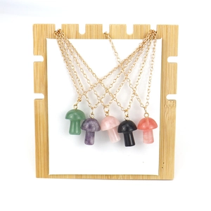 Five assorted natural stone mushroom pendants on gold chains displayed on bamboo board