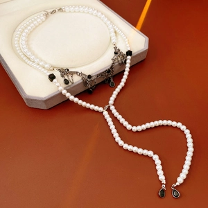 Detail view of pearl wing tassel necklace with black teardrop gemstone on velvet
