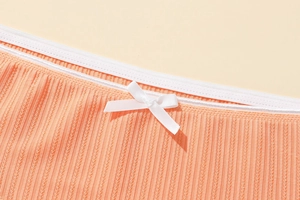 Close-up of coral knit panties featuring white lace elastic waistband and satin bow detail
