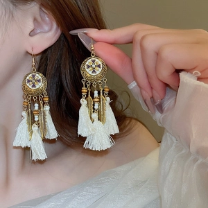 Detail of bohemian drop earrings featuring gold feathers and elegant white tassels