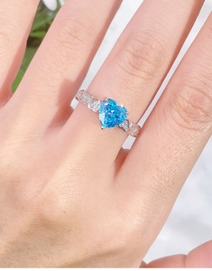 Macro shot of heart-shaped blue gemstone ring with hollow heart-patterned band on finger