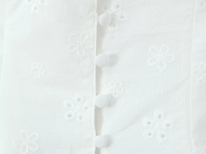 Detailed close-up of white lace eyelet floral embroidery with fabric-covered buttons